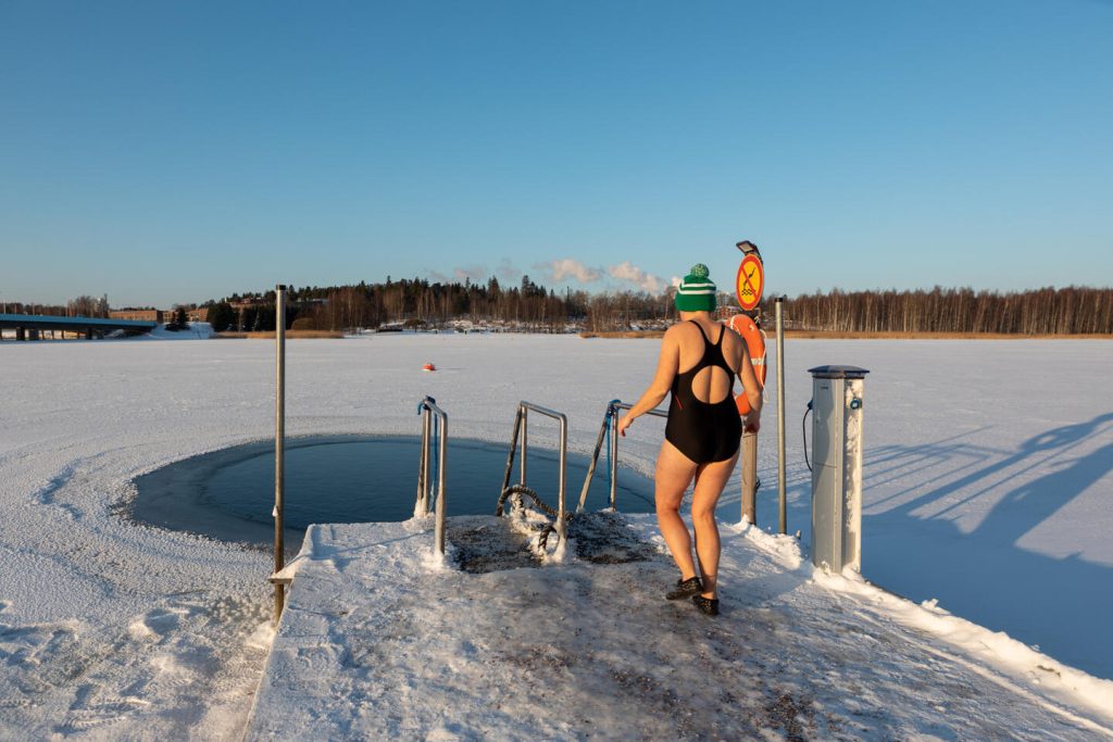 Henkilö laiturilla uimapuvussa ja pipo päässään astelee kohti avantoa.